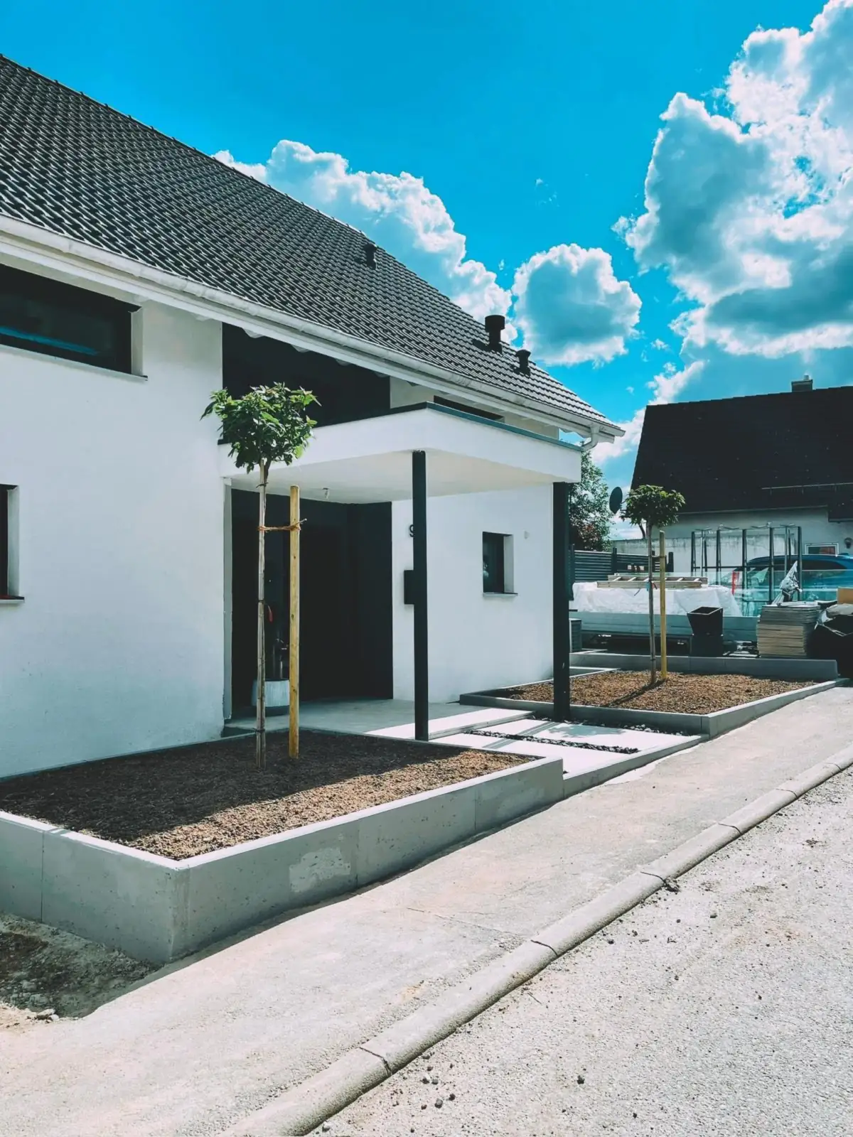 Neubau-Vorgarten mit Beton-Pflanzkästen und zwei jungen Bäumen