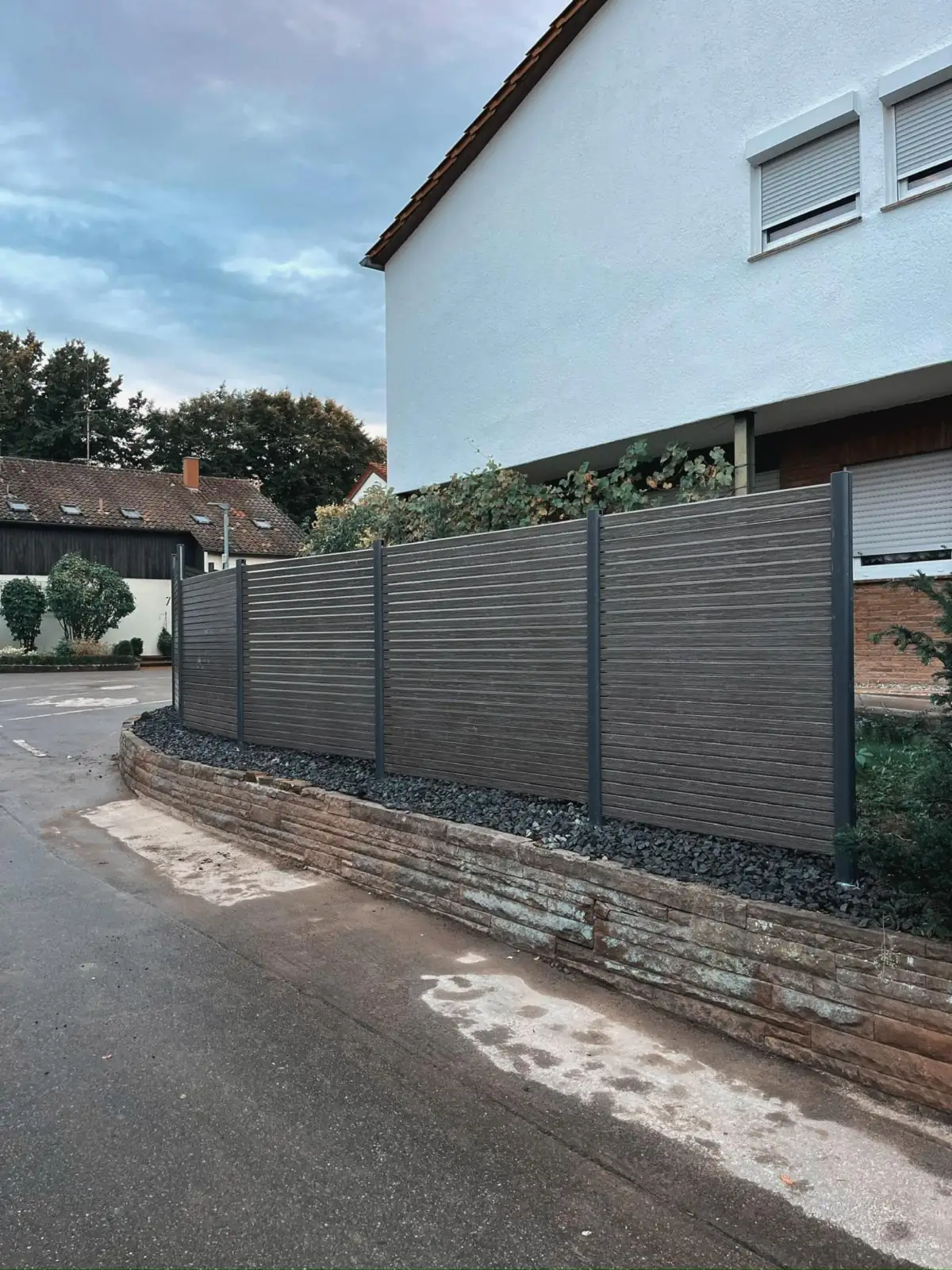 Sichtschutz aus WPC auf einer geschwungenen Natursteinmauer an der Straße